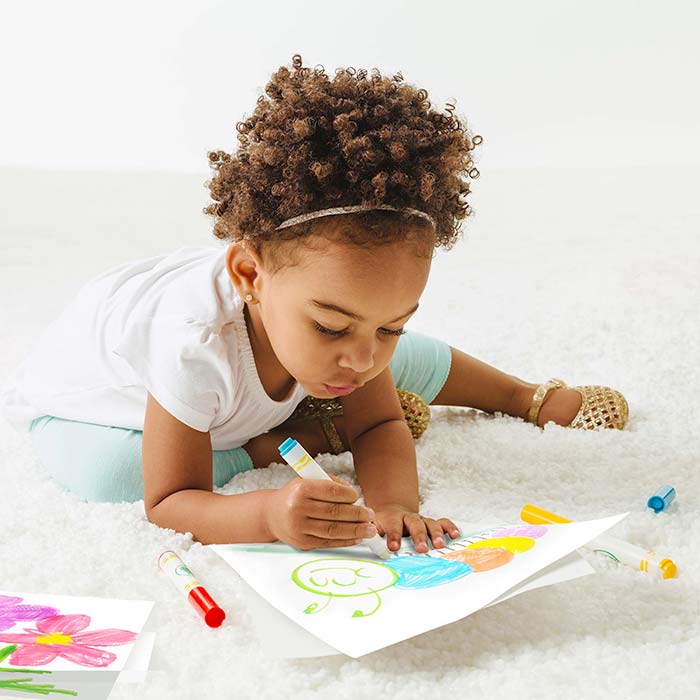 Young girl confidently colouring with crayola colour wonder mess free markers on a white carpet