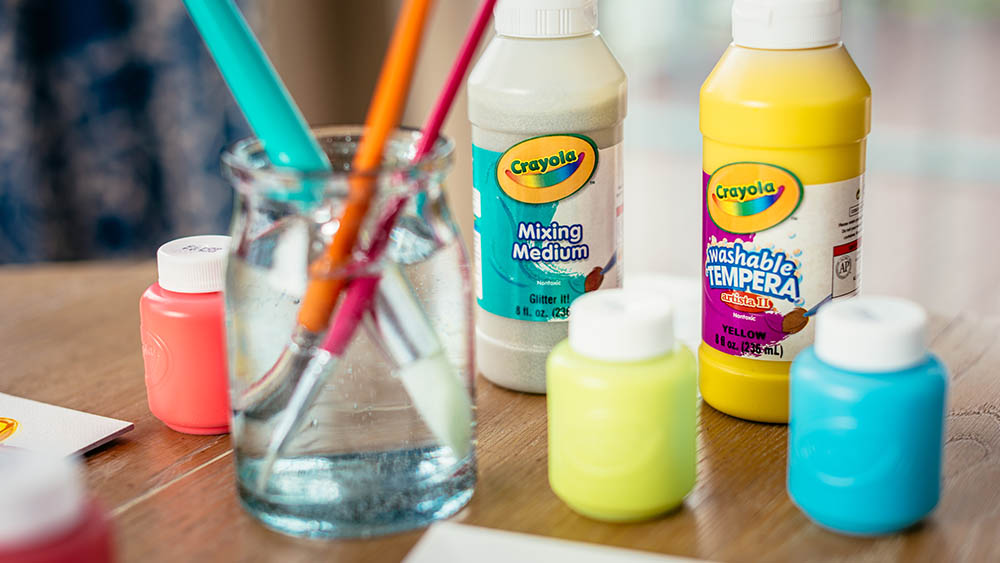 Dolores acrílicos y algunos pinceles en agua sobre un escritorio.